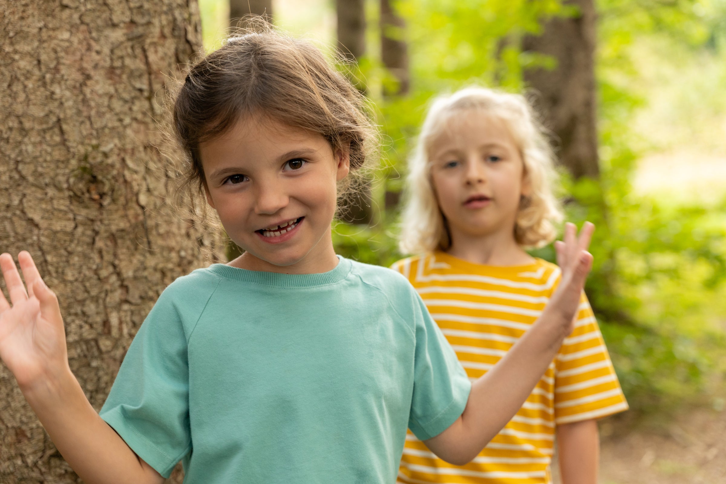 Zwei Mädchen im Wald mit einem türkisen und einem gelb-weiß gestreiften T-Shirt